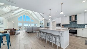 Uma cozinha moderna com uma ilha grande, banquetas e um espaço de refeições com sofá e mesa.