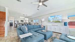 A spacious living room with a large sectional sofa, a dining area with a kitchen in the background, and a ceiling fan.
