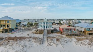A coastal residential area with houses, a sandy beach, and a wooden walkway leading to a blue house with a balcony.