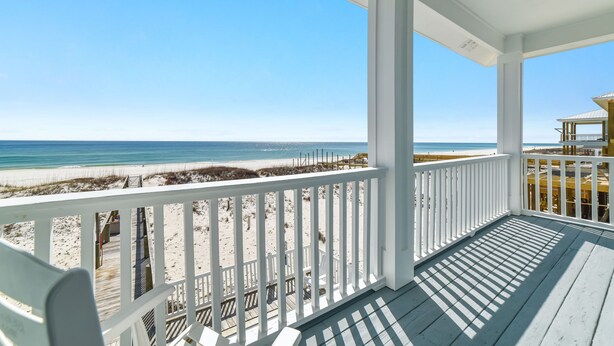A wooden deck with a white railing overlooking a beach.