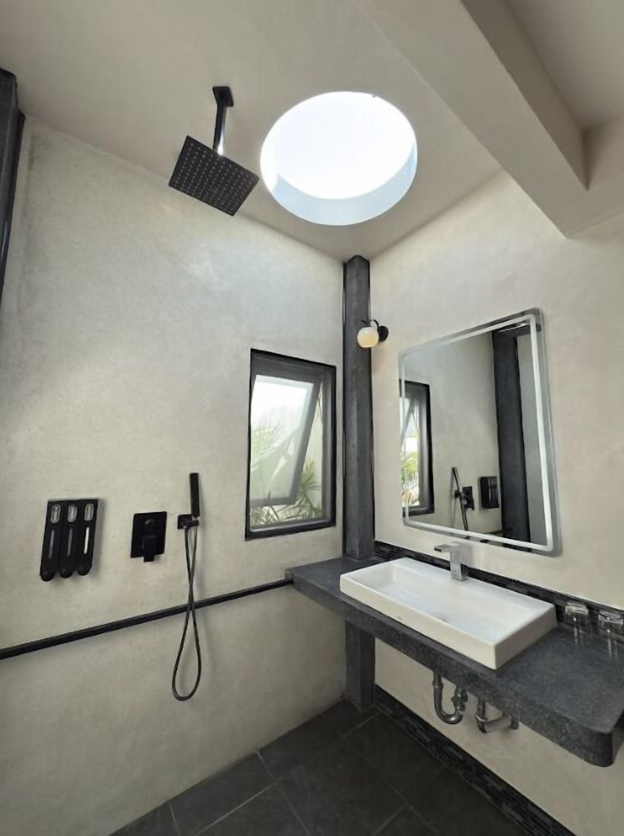 Un bagno moderno con uno specchio grande, una lampada a soffitto rotonda, una doccia e una finestra.