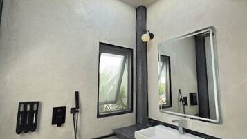 Un baño moderno con un espejo grande, una lámpara redonda en el techo, una ducha y una ventana.