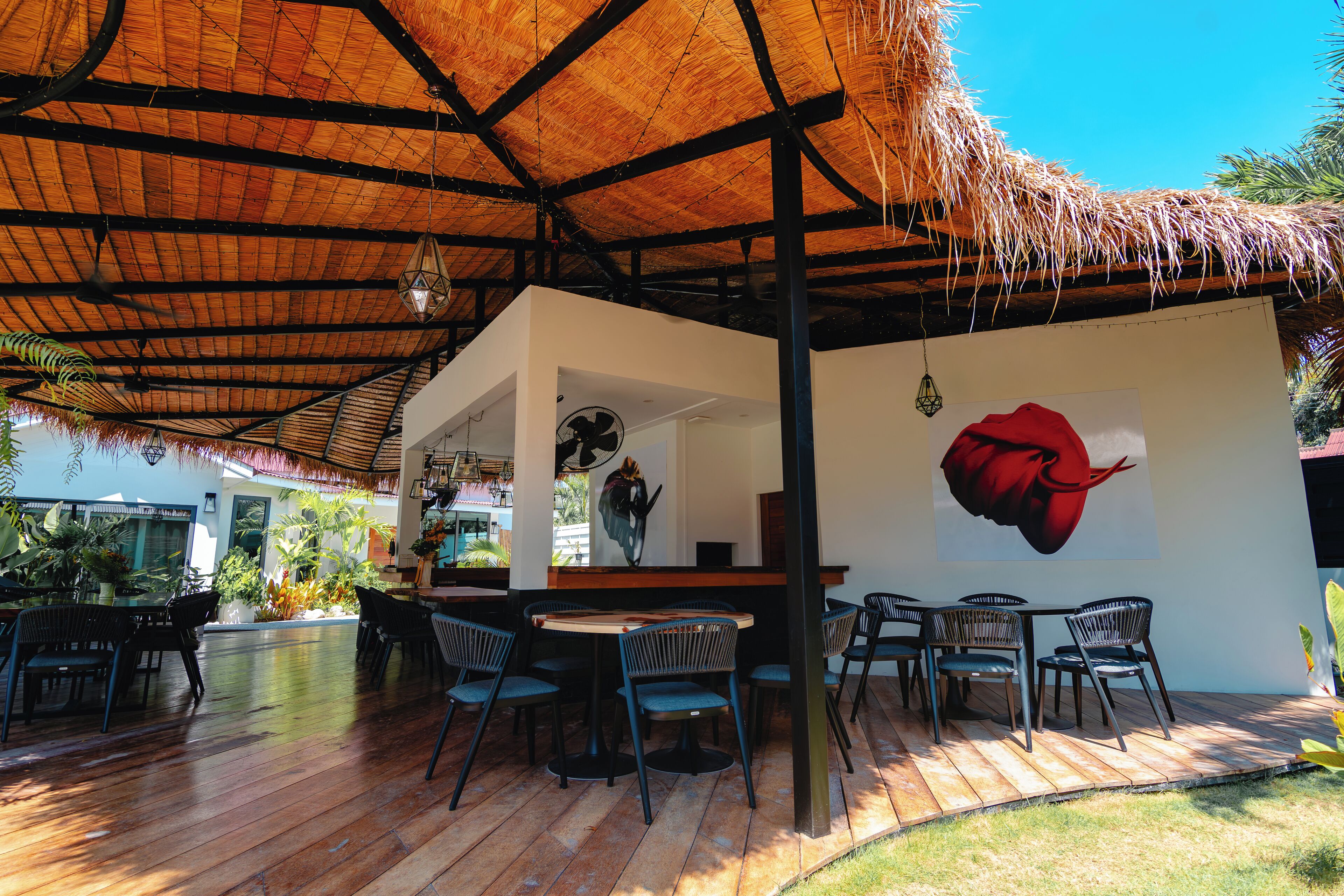 Un espace de restauration en plein air doté d’un toit de chaume, d’un plancher en bois et d’une fresque représentant une fleur rouge sur le mur.