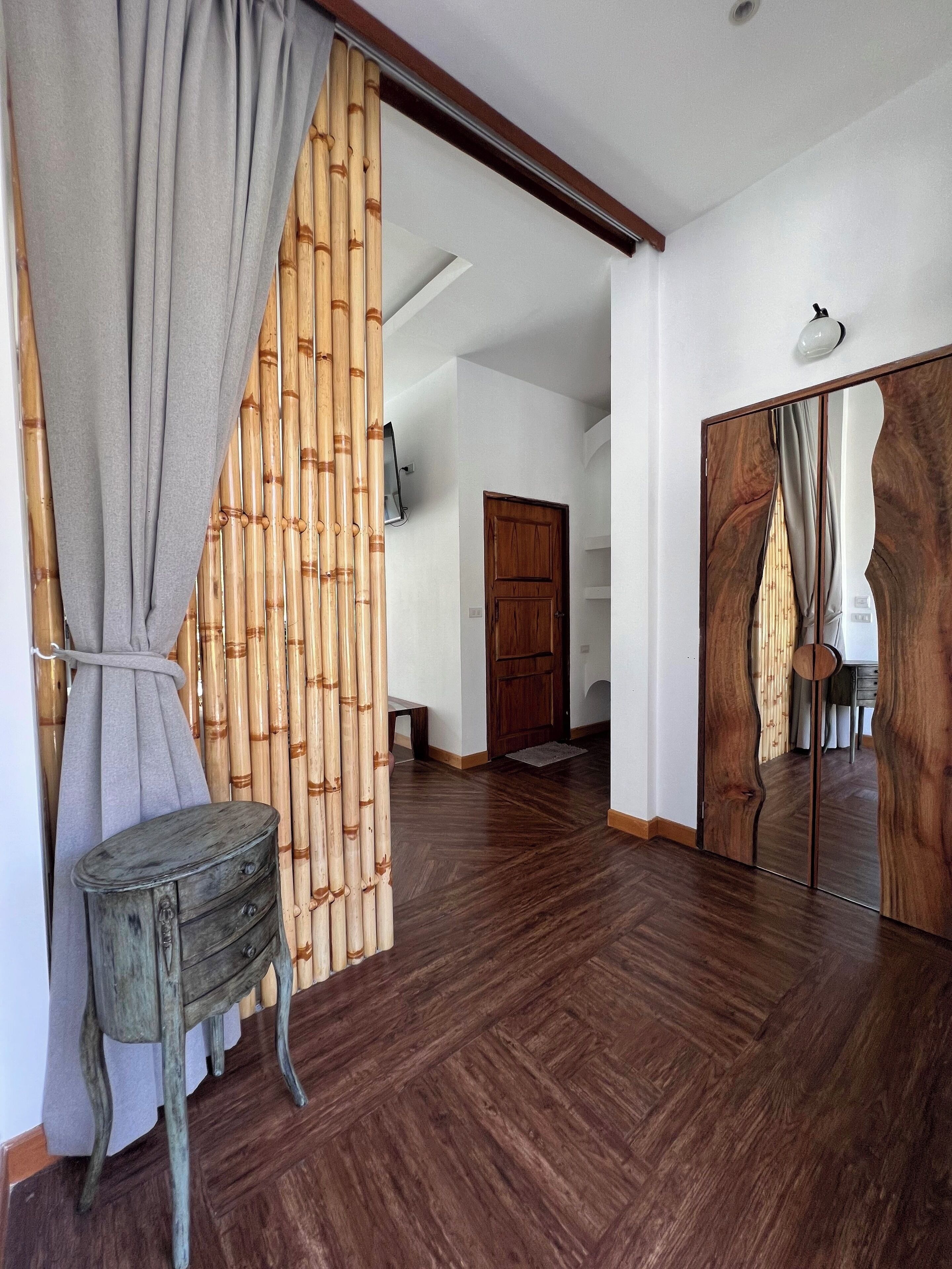 A room with a wooden floor, a wooden wardrobe, a mirror, and a grey curtain.
