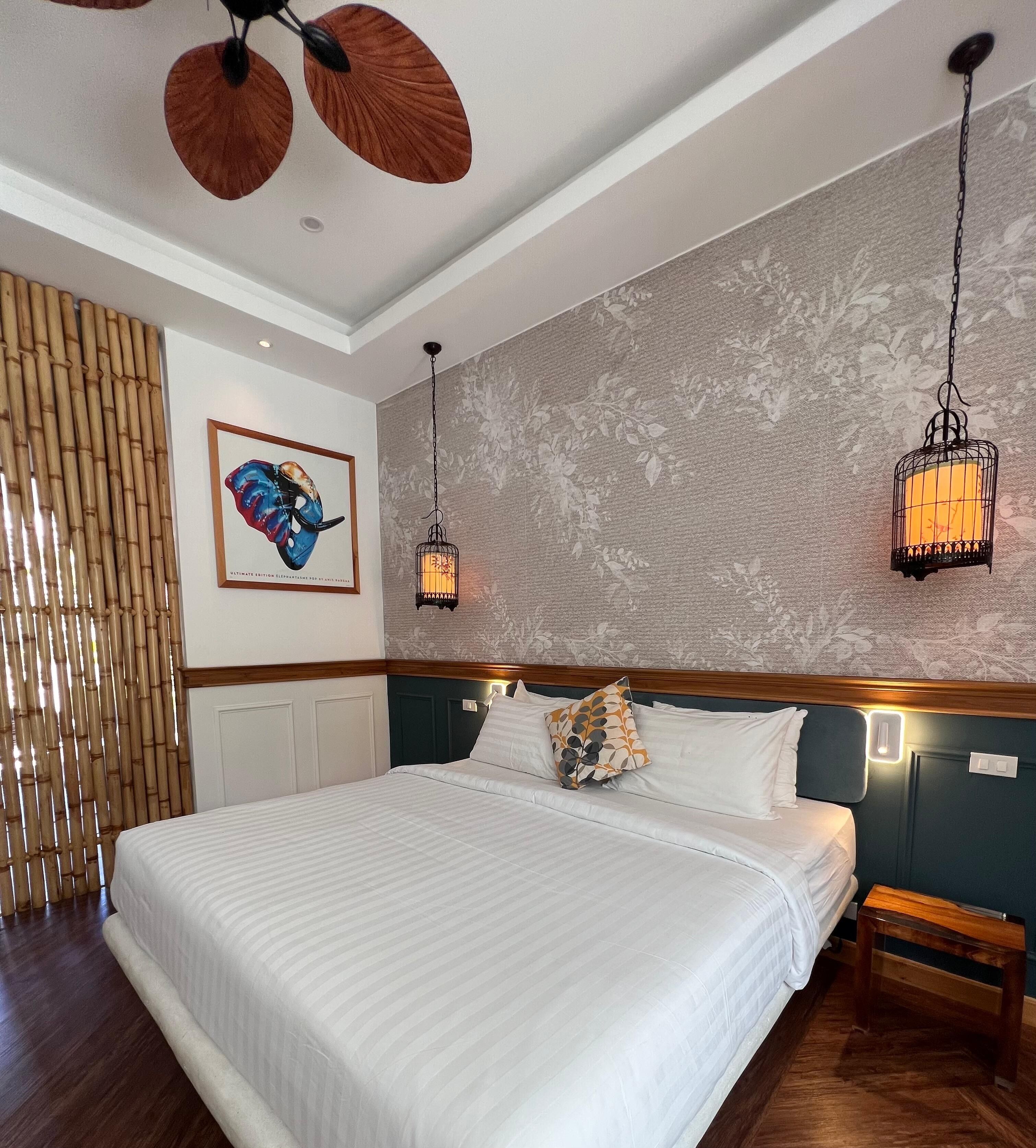 Een hotelkamer met een groot bed, twee wandlampen, een kunstwerk in een lijst en een bamboescherm.