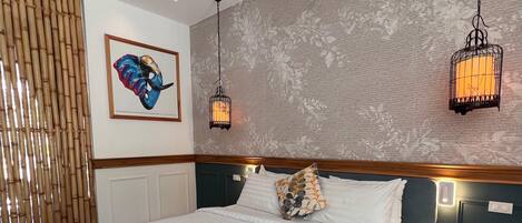 A hotel room with a large bed, two wall-mounted lamps, a framed artwork, and a bamboo screen.