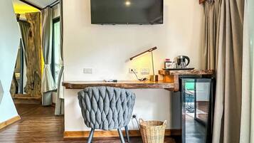 Habitación moderna con televisión de pantalla plana en la pared, un escritorio de madera con lámpara, una silla y un refrigerador pequeño.