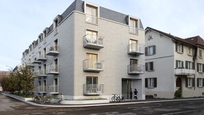 Ein modernes Mehrfamilienhaus mit Balkonen, einem Fahrradstellplatz und einem Fußweg.