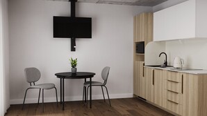 Eine moderne Küche mit schwarzem Arbeitsplatz, Holzschränken und einem eingebauten Backofen. Ein Essbereich mit zwei Stühlen und einem kleinen Tisch lädt zum Verweilen ein, und auf dem Tisch steht ein Blumentopf.