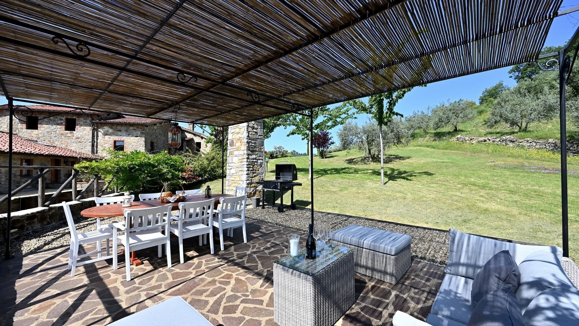An outdoor patio with stone flooring, white furniture, and a pergola overhead.