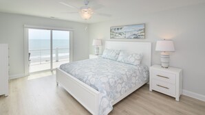 A bedroom with a large bed, two bedside tables with lamps, a ceiling fan, and a view of the ocean through a sliding glass door. - Oceanfront 7 BR Beach House with a Private Pool! Sandy Days (Surfside Beach)