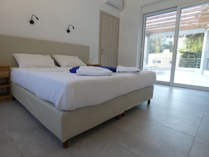 Ein modernes Schlafzimmer mit einem großen Bett, einem Nachttisch aus Holz und einer Glastür, die zu einem Außenbereich führt.