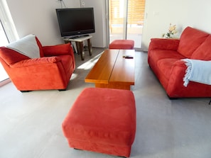 Ein Wohnzimmer mit einem Flachbildfernseher auf einem Schrank, zwei roten Sofas, einem Holztisch und einem kleinen Hocker.