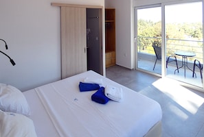 Een hotelkamer met een bed, een kledingkast, een balkon met een tafel en stoelen, en uitzicht op bomen.