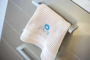 Een beige handdoek met een logo hangt aan een metalen handdoekhouder.