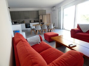Ein modernes Wohnzimmer mit roten Sofas, einem Holztisch und einem Essbereich mit grauen Stühlen.