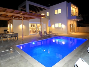 Een modern huis met een zwembad, buitenmeubels en een overdekt terras.