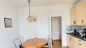 Eine kleine Küche mit Holzausstattung, einem Esstisch mit Stühlen, einer Pendelleuchte und einem gerahmten Bild an der Wand.