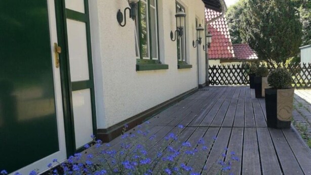 Eine Holzterrasse mit einem weißen Gebäude, das grüne Verzierungen und Fenster mit grünen Fensterbänken aufweist.