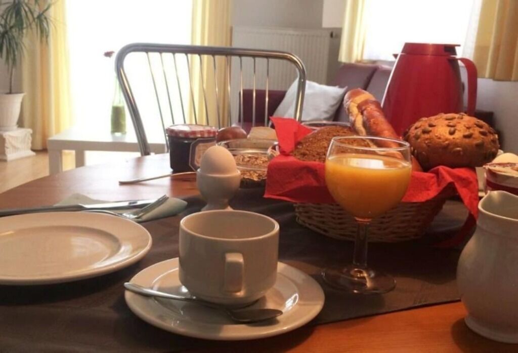 Een ontbijttafel gedekt voor twee personen, met borden, een kopje, een glas sinaasappelsap, een muffin en een mand met brood.