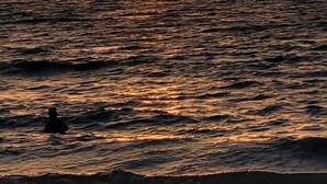 Un coucher de soleil sur une étendue d’eau, avec la silhouette d’une personne à l’horizon.