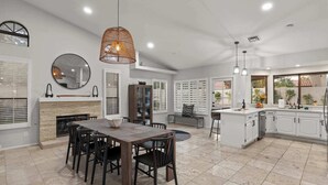 A spacious kitchen with white cabinets, a dining area with a large table and chairs, and a hanging pendant light. - Backyard Bliss: Firepit, Putt, Play, Pool & Spa! (Scottsdale)