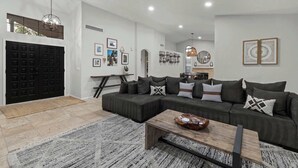 A modern living room with a sectional sofa, a coffee table, and a dining area in the background. - Backyard Bliss: Firepit, Putt, Play, Pool & Spa! (Scottsdale)