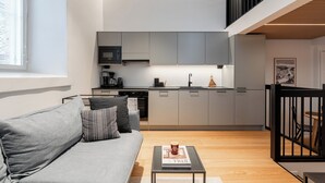 A modern kitchen with grey cabinets, a black countertop, and a dining area with a black railing.