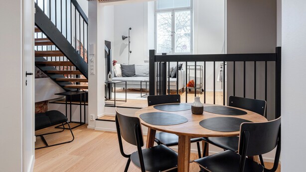 A modern interior with a staircase, a dining area with a round table and black chairs, and a sofa in the background.