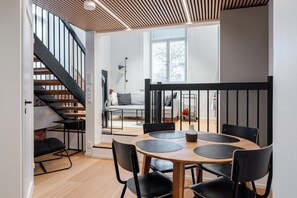 Un interior moderno con una escalera, un área de comedor con una mesa redonda y sillas negras, y un sofá al fondo.
