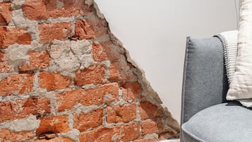 A room with a brick wall, a flat-screen TV mounted on the wall, and a grey sofa with a white cushion.