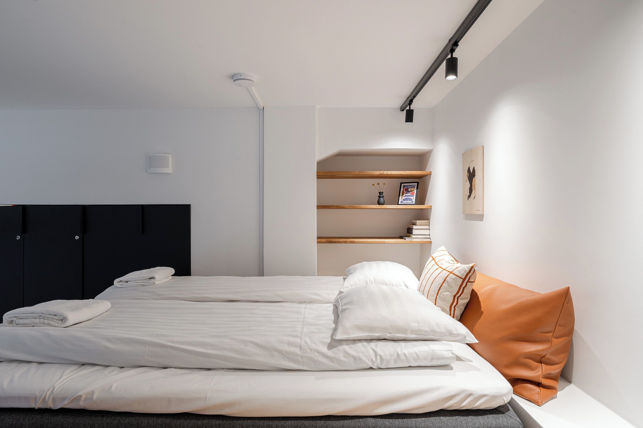 Ein modernes Schlafzimmer mit Bett, Kleiderschrank, einer Bücherablage und einer Wandleuchte.