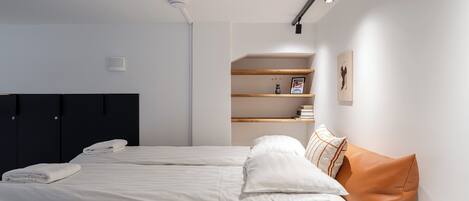 A modern bedroom with a bed, a wardrobe, a shelf with books, and a wall-mounted light fixture.