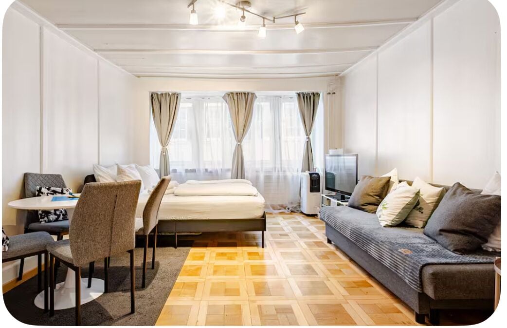 A hotel room with a bed, a sofa, a desk with chairs, and a TV.
