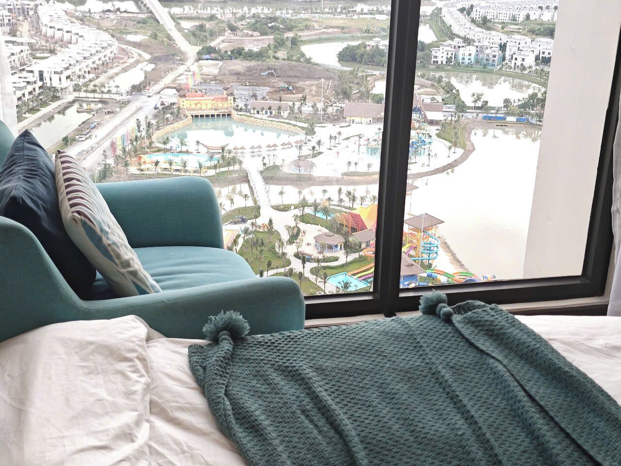 A hotel room with a large window offering a view of a cityscape, including a river and a park.