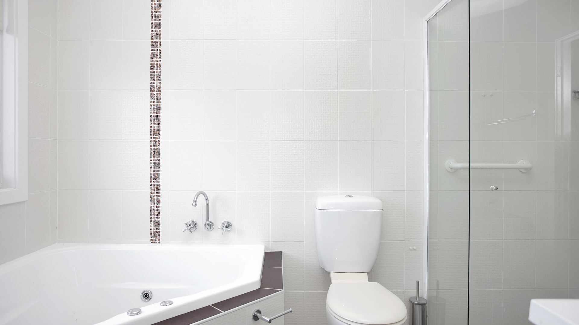 A modern bathroom with a bathtub, toilet, and glass shower enclosure.
