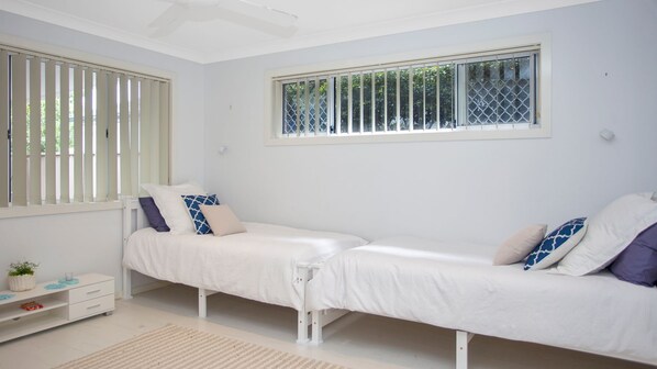 A bedroom with two single beds, a small bedside table, a nightstand, and a window with blinds.