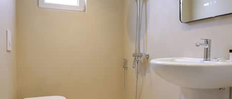 A modern bathroom with a toilet, shower, sink, and a window.