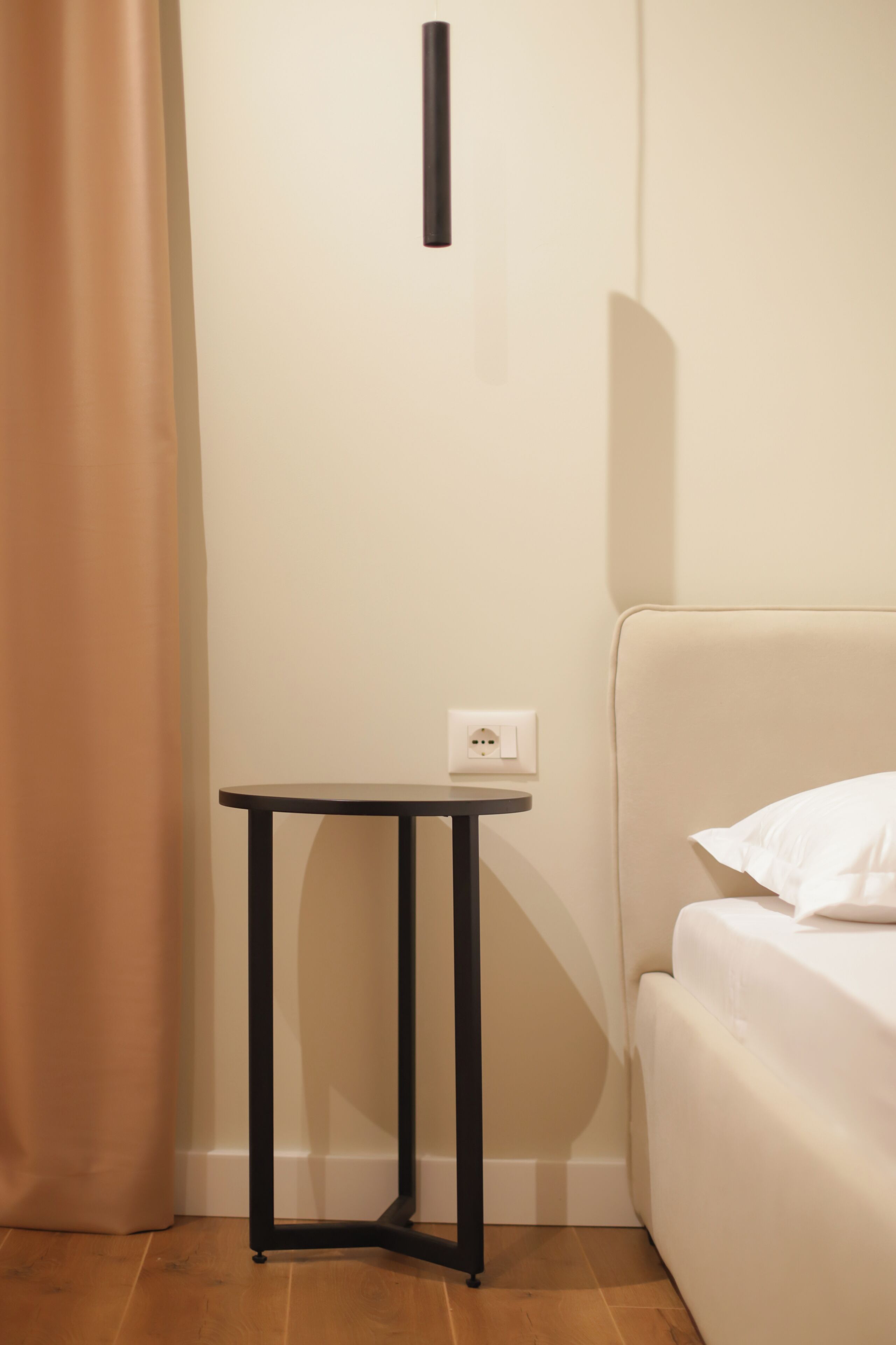 A corner of a room with a bed, a small table, and a power outlet on the wall.