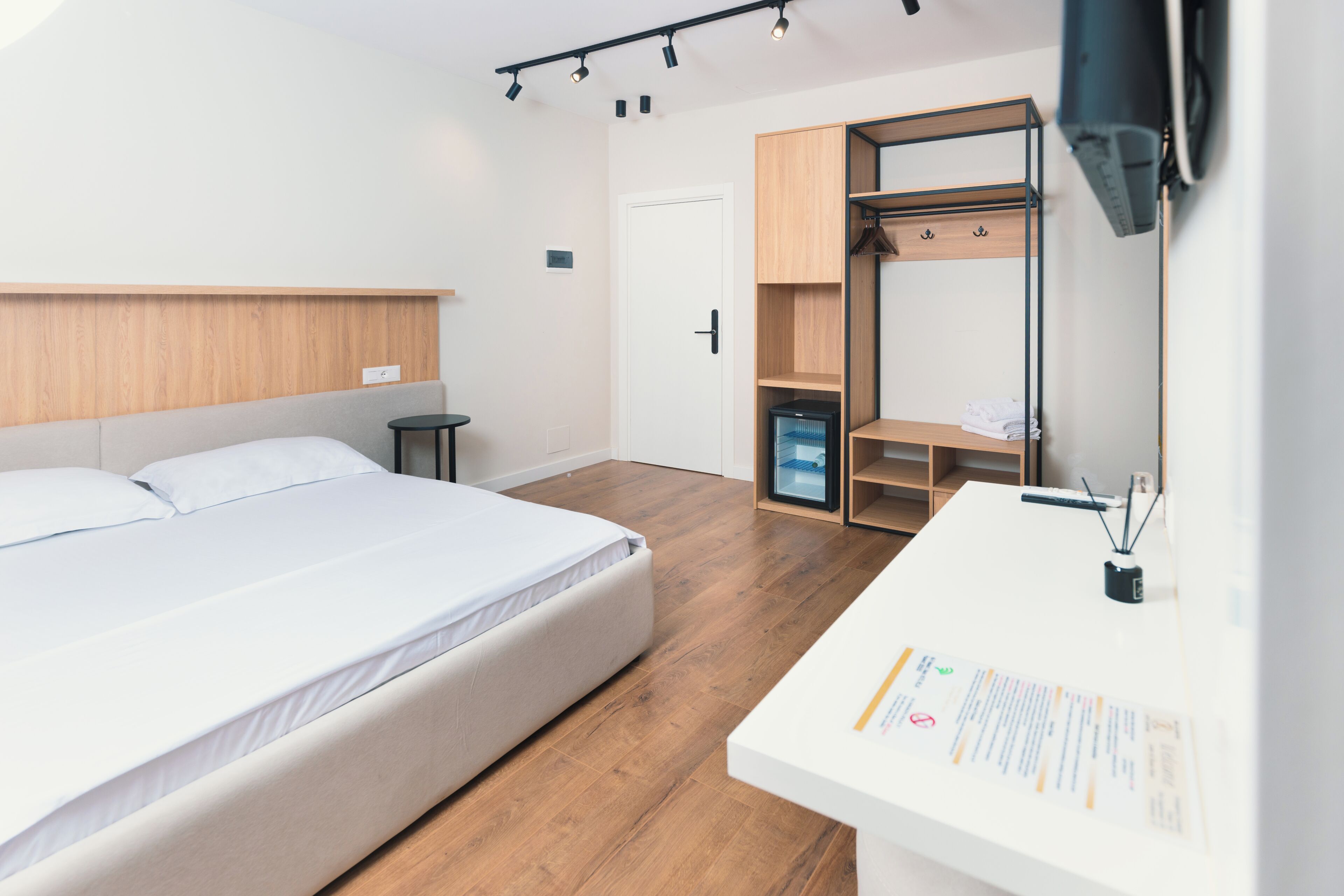 Una habitación de hotel moderna con una cama, un escritorio, un armario y un televisor instalado en la pared.