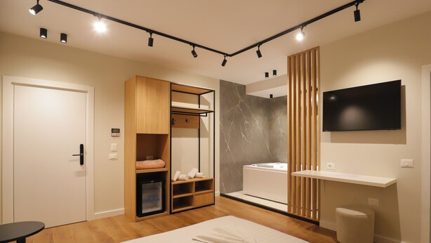 Una habitación de hotel moderna con una cama, un armario con espejo, un tocador con lavabo y un televisor montado en la pared.