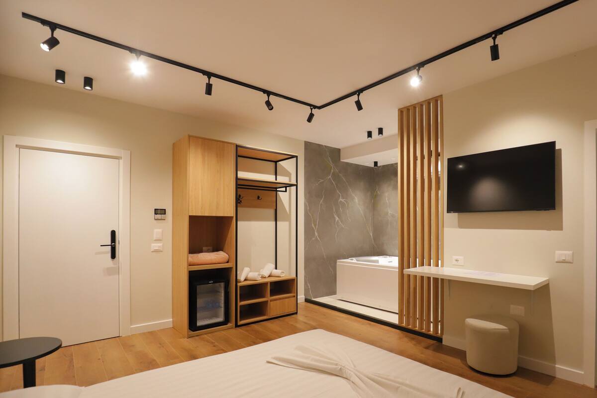 A modern hotel room with a bed, a wardrobe with a mirror, a vanity with a sink, and a TV mounted on the wall.