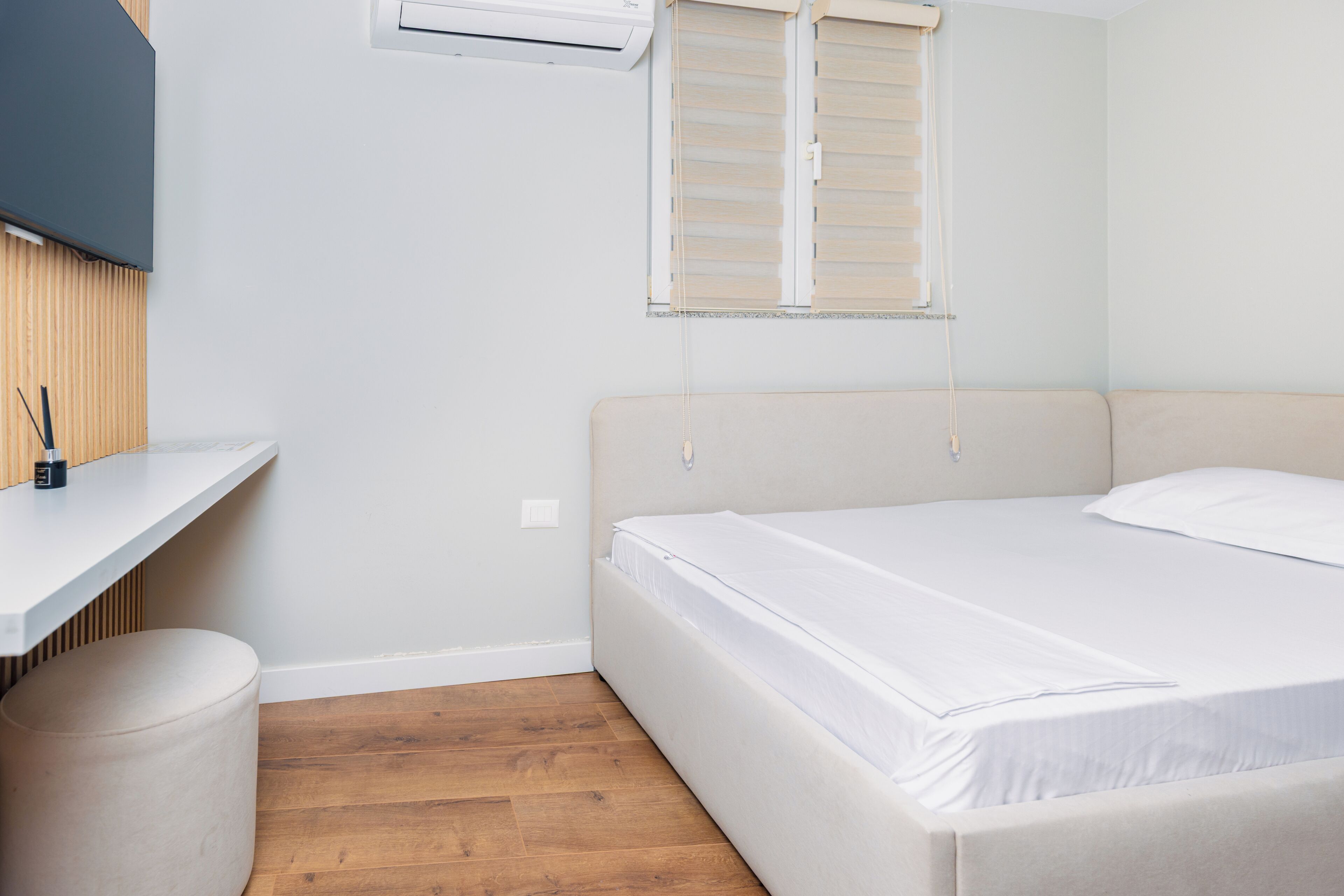 A bedroom with a bed, a desk, a chair, and a window with blinds.