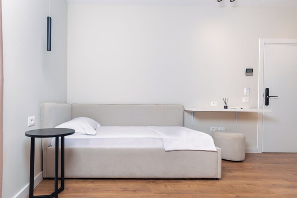 A minimalist room with a bed, a small round table, a bench, and a door. - Hotel Relax City Center (Tirana)