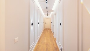 Un pasillo estrecho con paredes blancas y suelo de madera, que conduce a una puerta con el número 110.