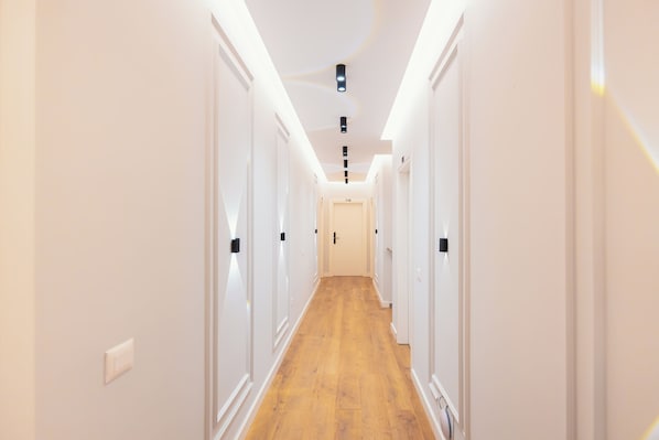 A narrow hallway with white walls and wooden flooring, leading to a door marked '110'. - Hotel Relax City Center (Tirana)