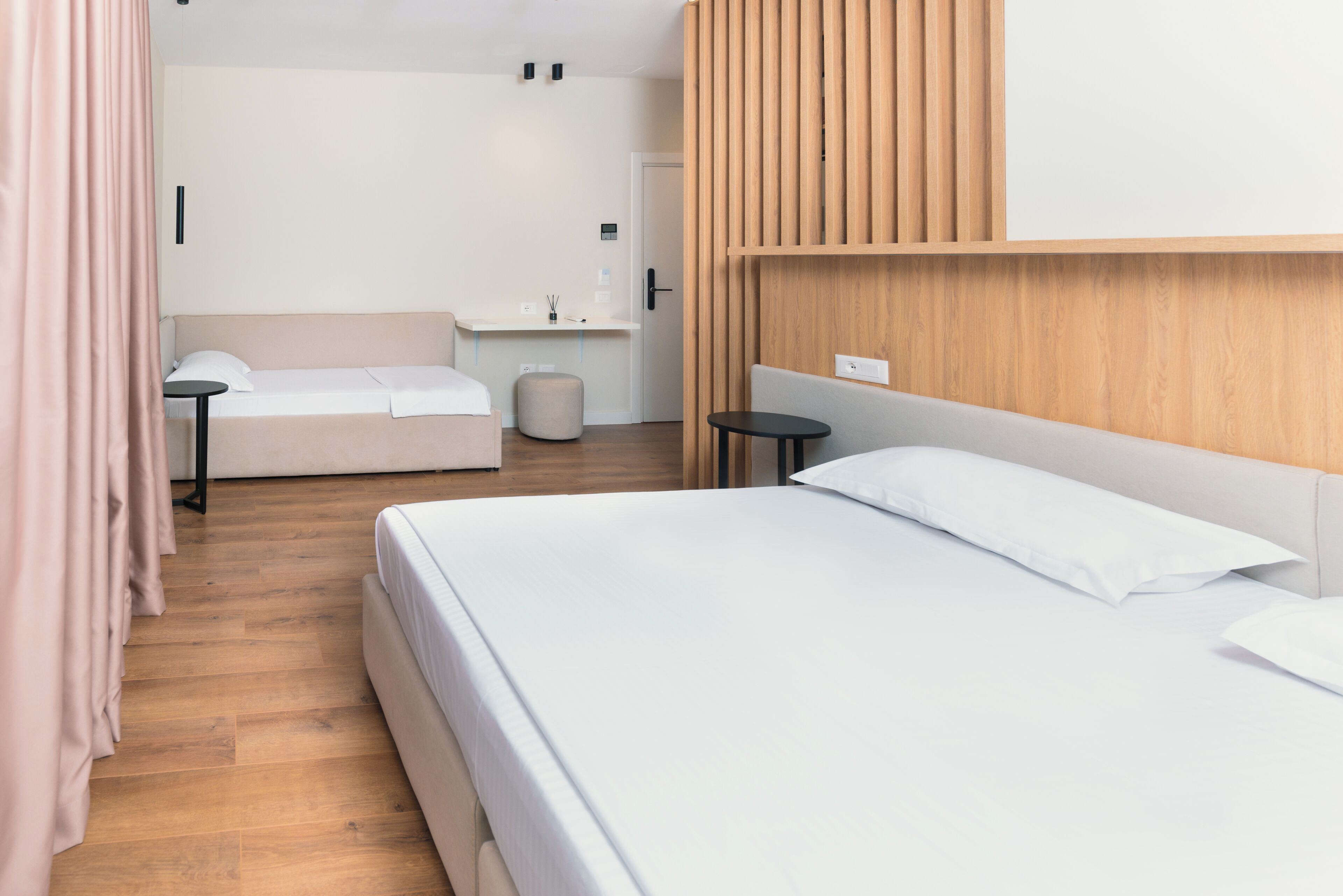 Habitación de hotel con una cama grande, una cama más pequeña, un escritorio, una silla y un panel de pared de madera.