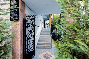 A staircase leading to a hotel entrance with directional signs, a metal gate, and surrounding greenery. - Hotel Relax City Center (Tirana)