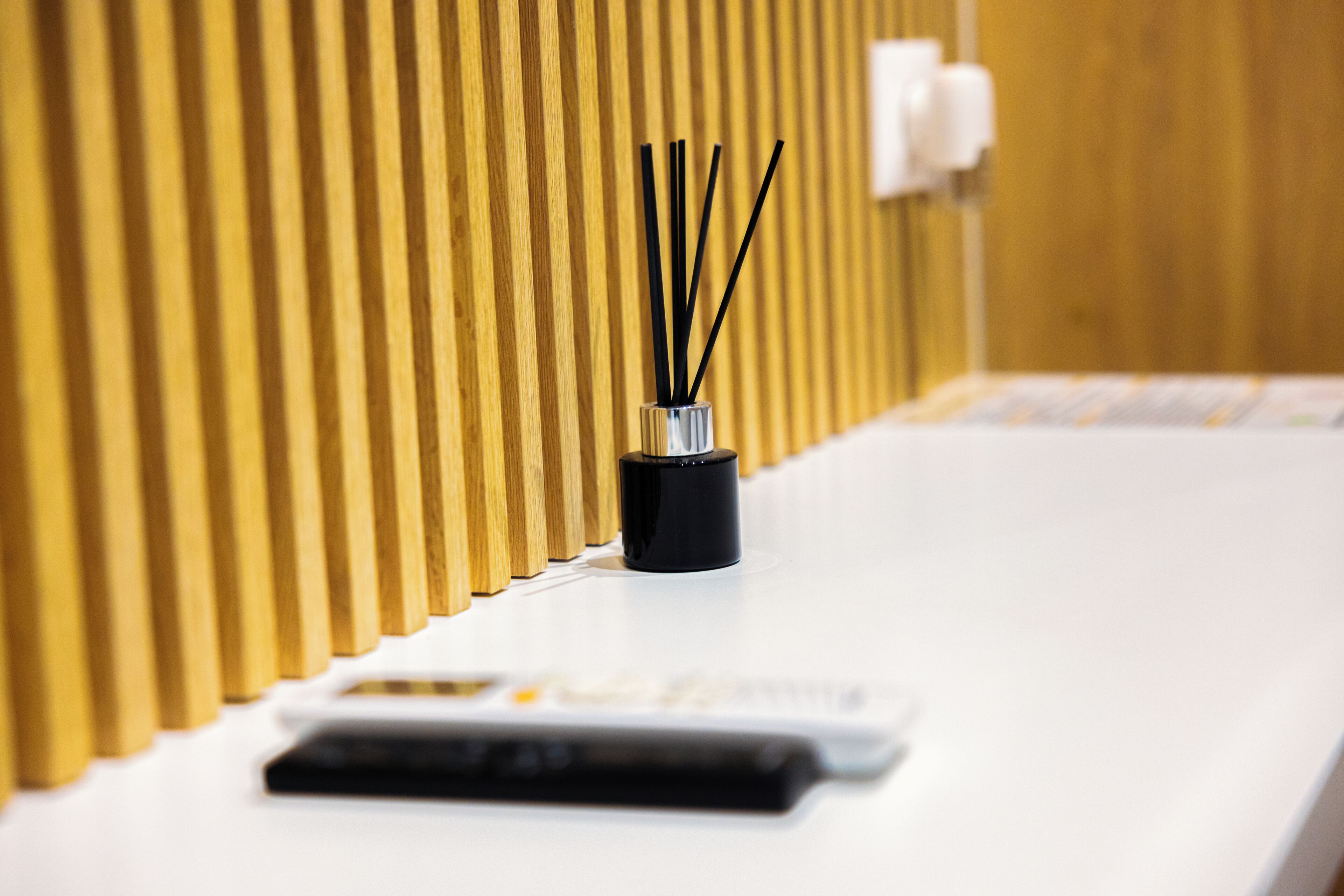 A white reception desk with a black vase containing black sticks, a white switchboard, and a wooden panel wall.
