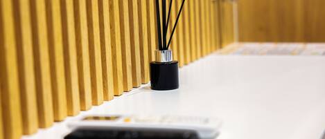 A white reception desk with a black vase containing black sticks, a white switchboard, and a wooden panel wall.